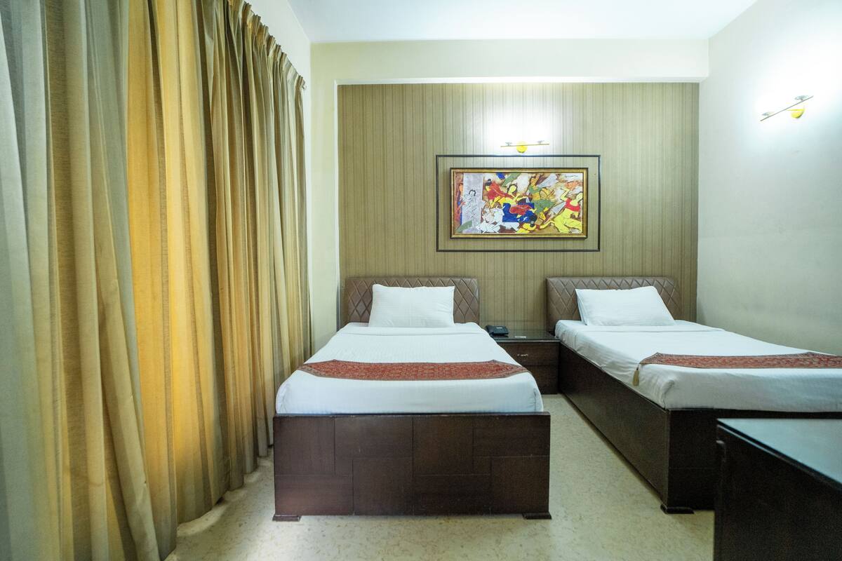 Ein Hotelzimmer mit zwei Betten, einem Nachttisch, einem Bild an der Wand und einem Vorhang.