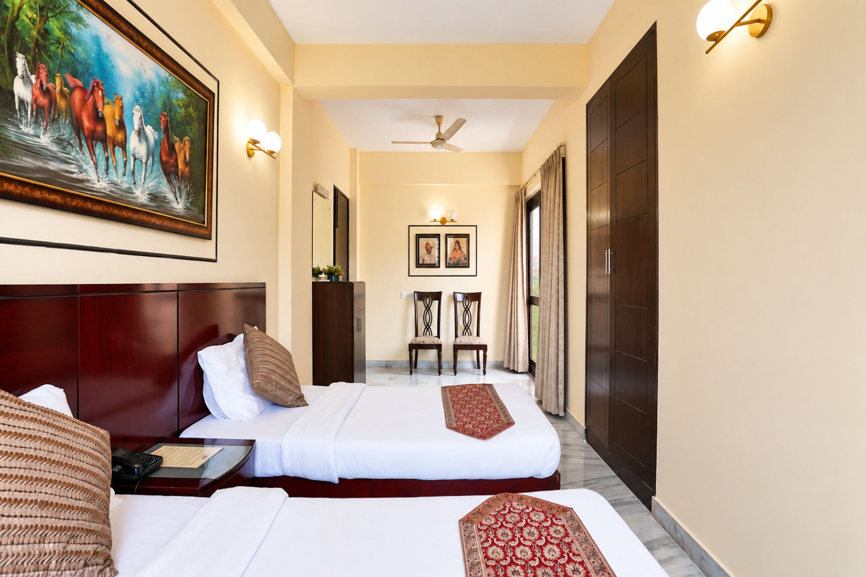 A hotel room with a large bed, a smaller bed, a desk, a chair, a painting, and a wardrobe.