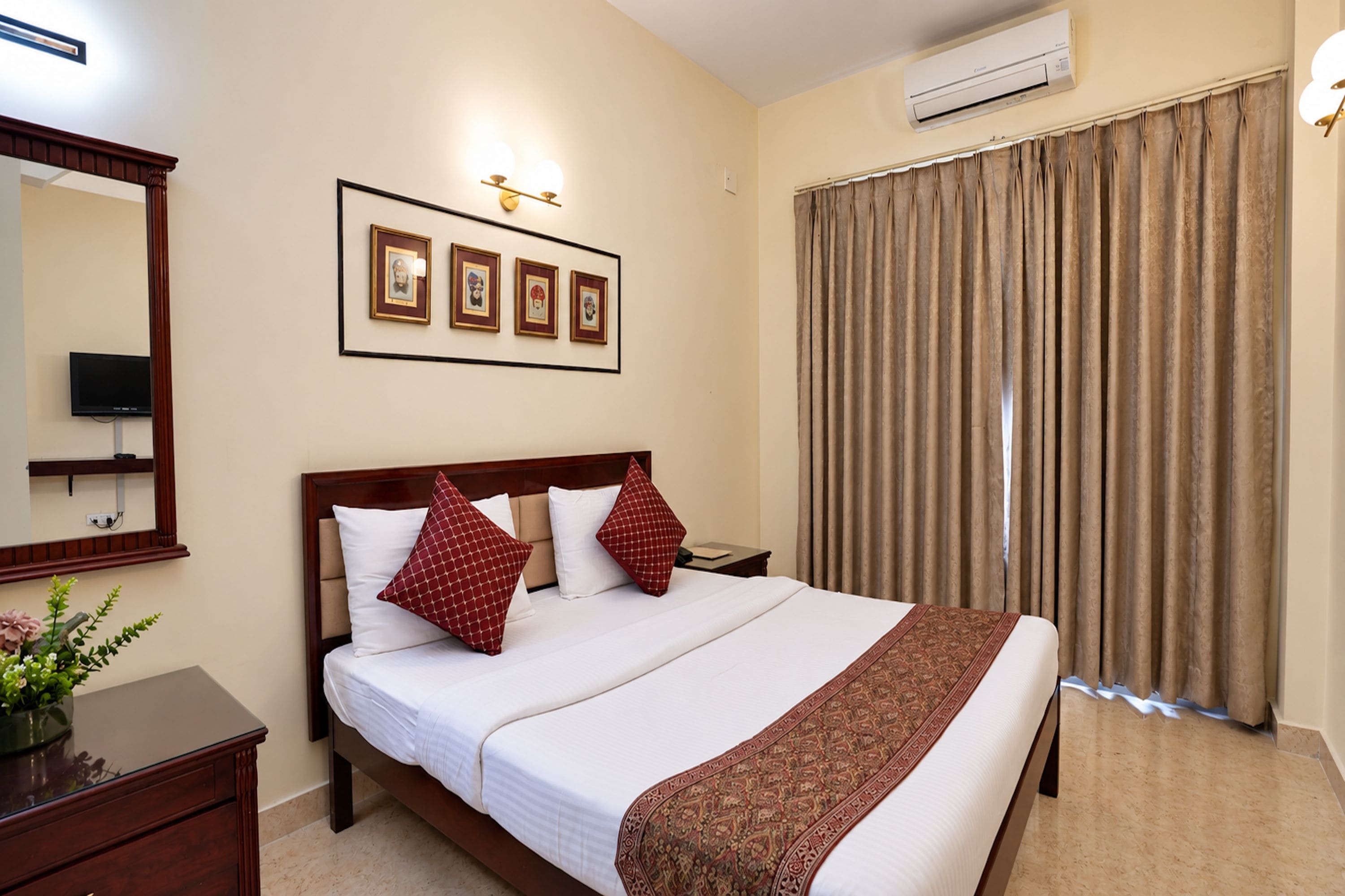 A hotel room with a bed, a bedside table, a mirror, a wall-mounted air conditioner, and a window with curtains.
