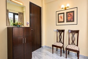 Una habitación con armario, dos sillas, un espejo e iluminación en la pared.