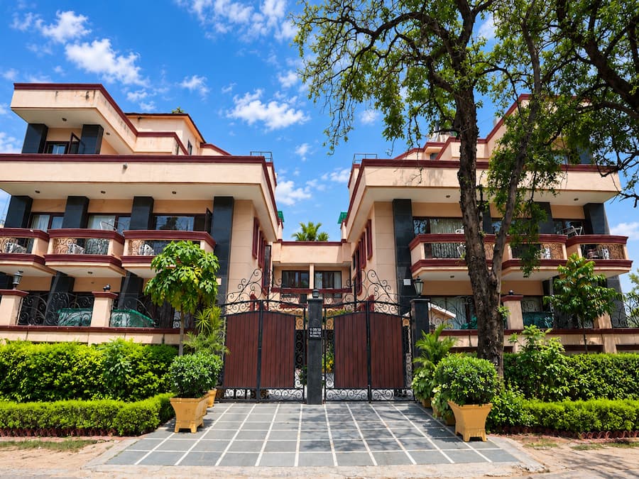 A multi-story residential building with a gated entrance, surrounded by greenery and a clear sky.