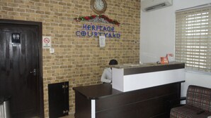 Un mostrador de recepción con un reloj encima, un cartel que dice 'Heritage Courtyard', un letrero de 'no fumar' y una ventana con persianas.