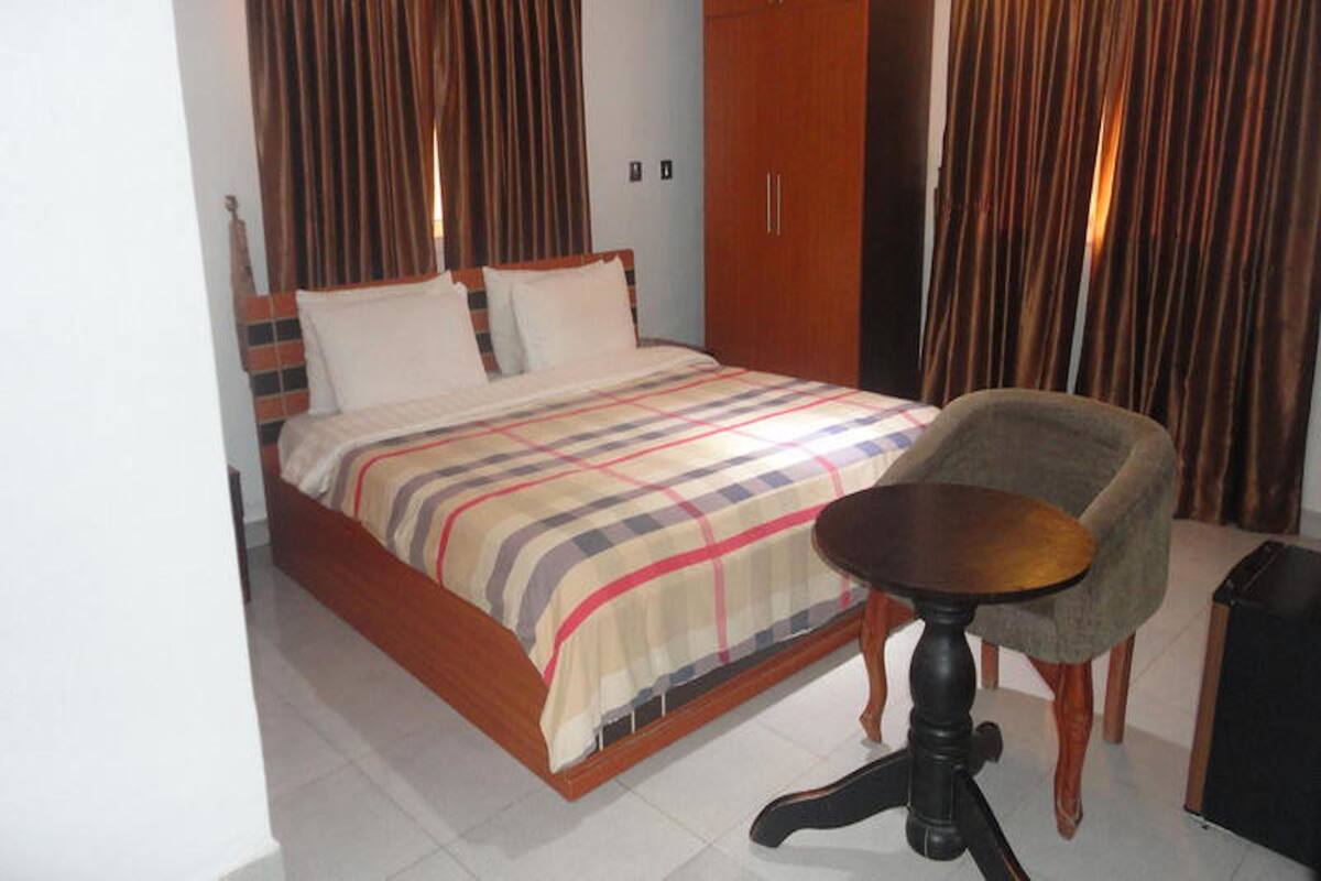 A bedroom with a bed, a chair, a small table, and a wardrobe.