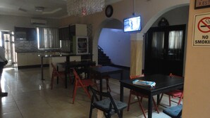 Un comedor con televisión, un cartel de prohibido fumar y una cocina al fondo.