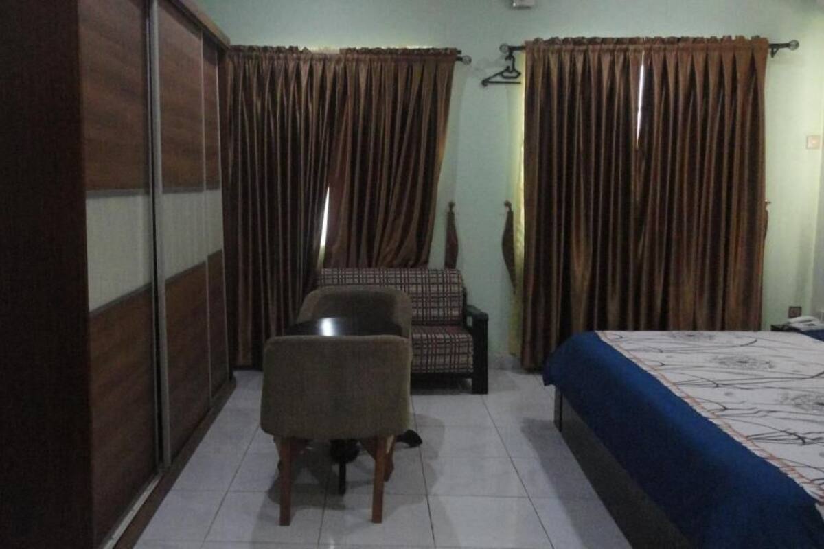 A bedroom with a bed, a chair, a wardrobe, and curtains.