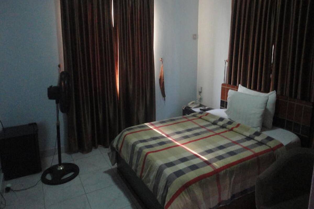 A bedroom with a bed, curtains, a nightstand, and a speaker.
