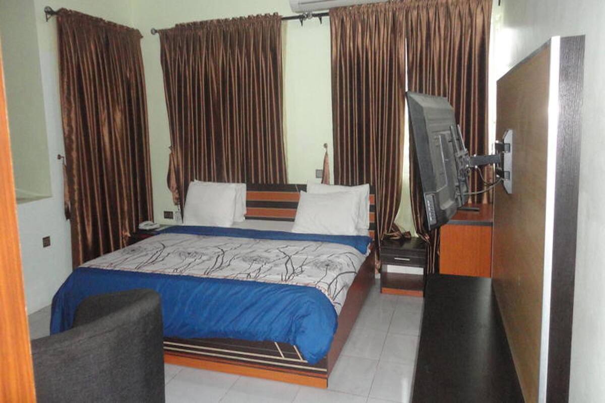 A hotel room with a bed, curtains, a TV, and a desk.