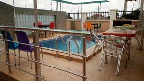 Una piscina al aire libre con barandales metálicos, rodeada de sillas y mesas de colores.