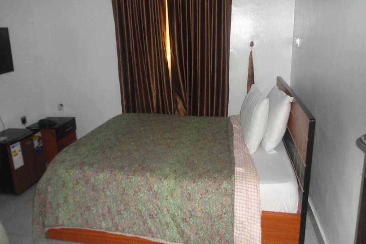 A standard hotel room with a single bed, a desk with a chair, a curtain, and a television mounted on the wall.