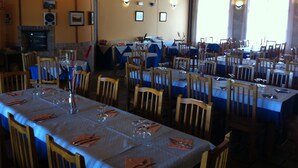 Un restaurante con varias mesas listas para comer, sillas de madera y una pared de ladrillo con cuadros enmarcados.
