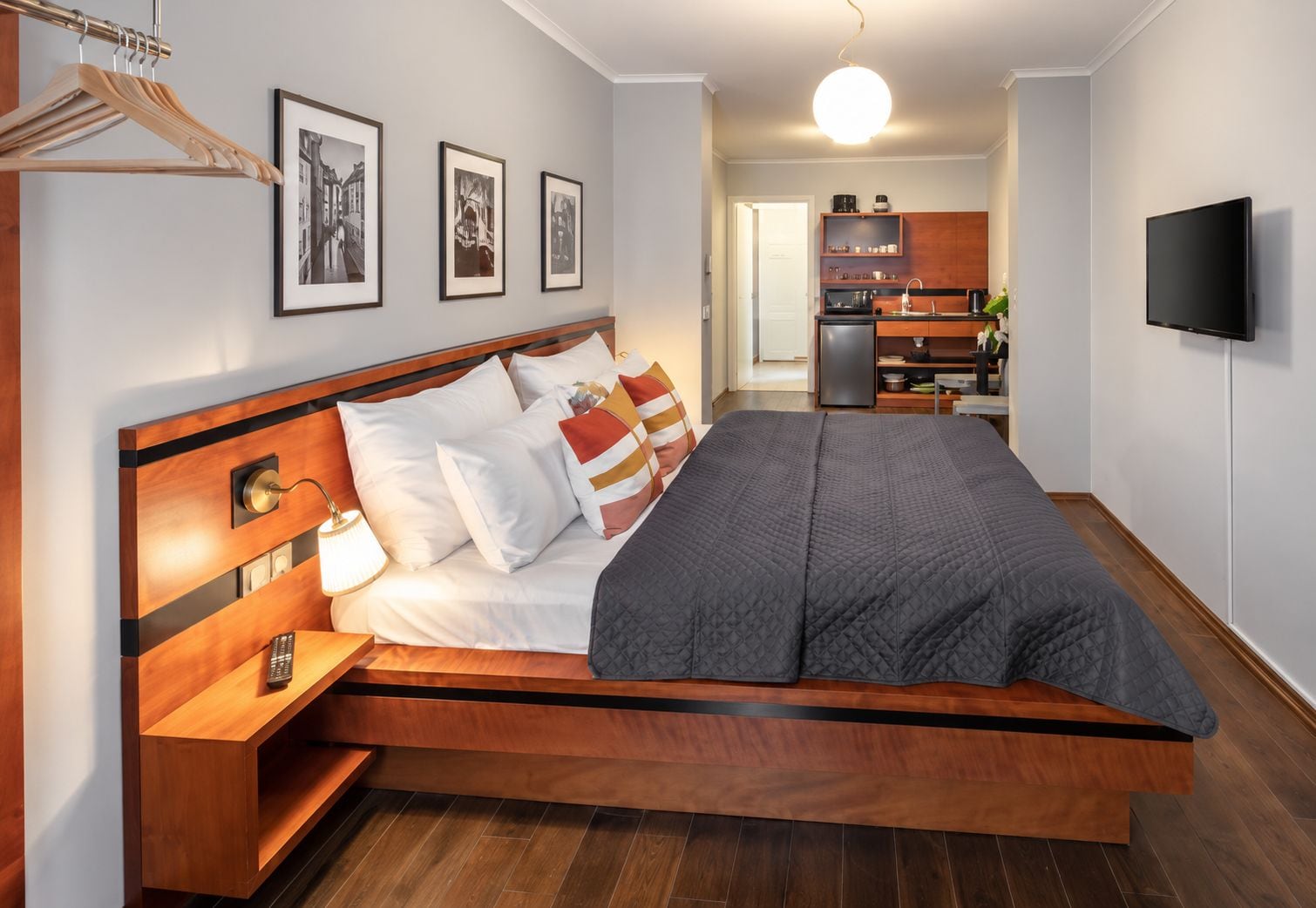 Un dormitorio moderno con una cama de madera, una mesita de noche y un televisor montado en la pared.