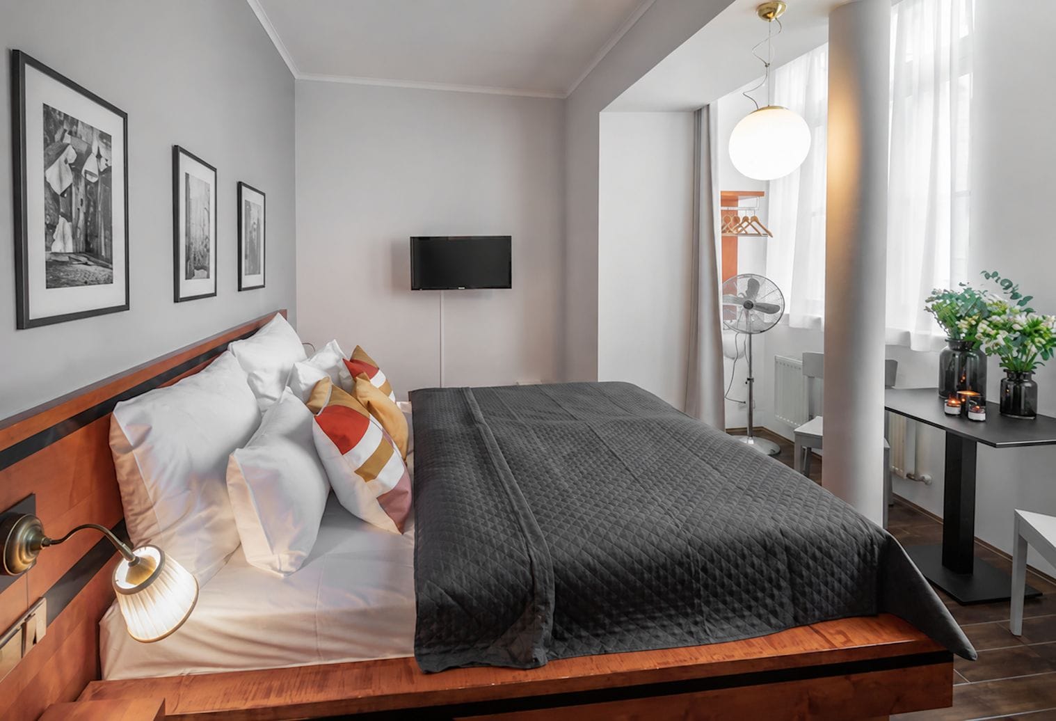 Un dormitorio moderno con cama, mesita de noche, lámpara, televisor de pared y cuadros enmarcados.