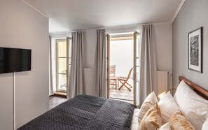 Habitación de hotel con cama, televisor, balcón con una silla y ventana con cortinas.