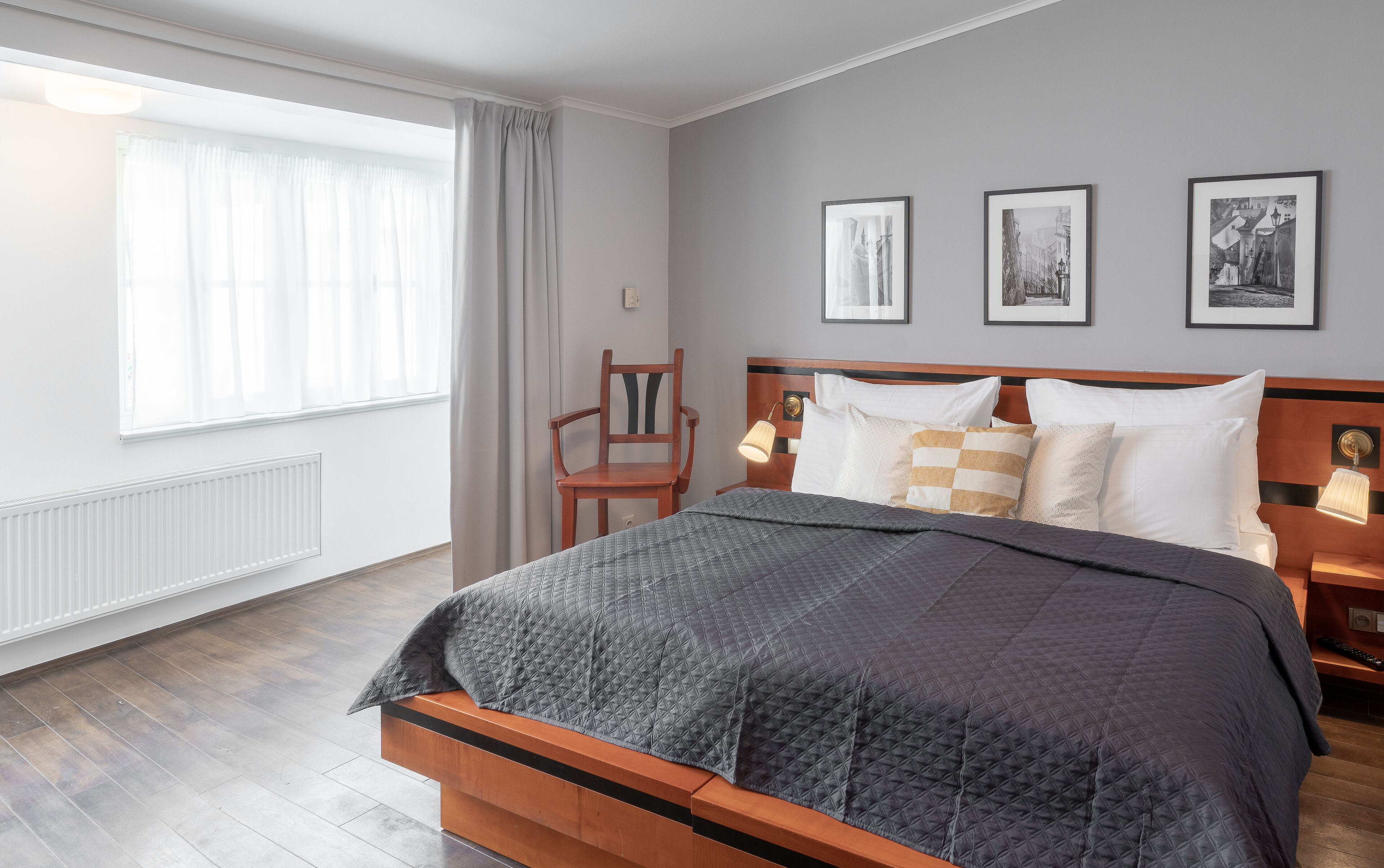Habitación de hotel ordenada con una cama grande, una silla, una mesita de noche con lámpara y tres cuadros en la pared.