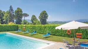 A swimming pool with blue lounge chairs and a table with umbrellas, surrounded by hedges and trees. - Podere Grossi (Borgo San Lorenzo)