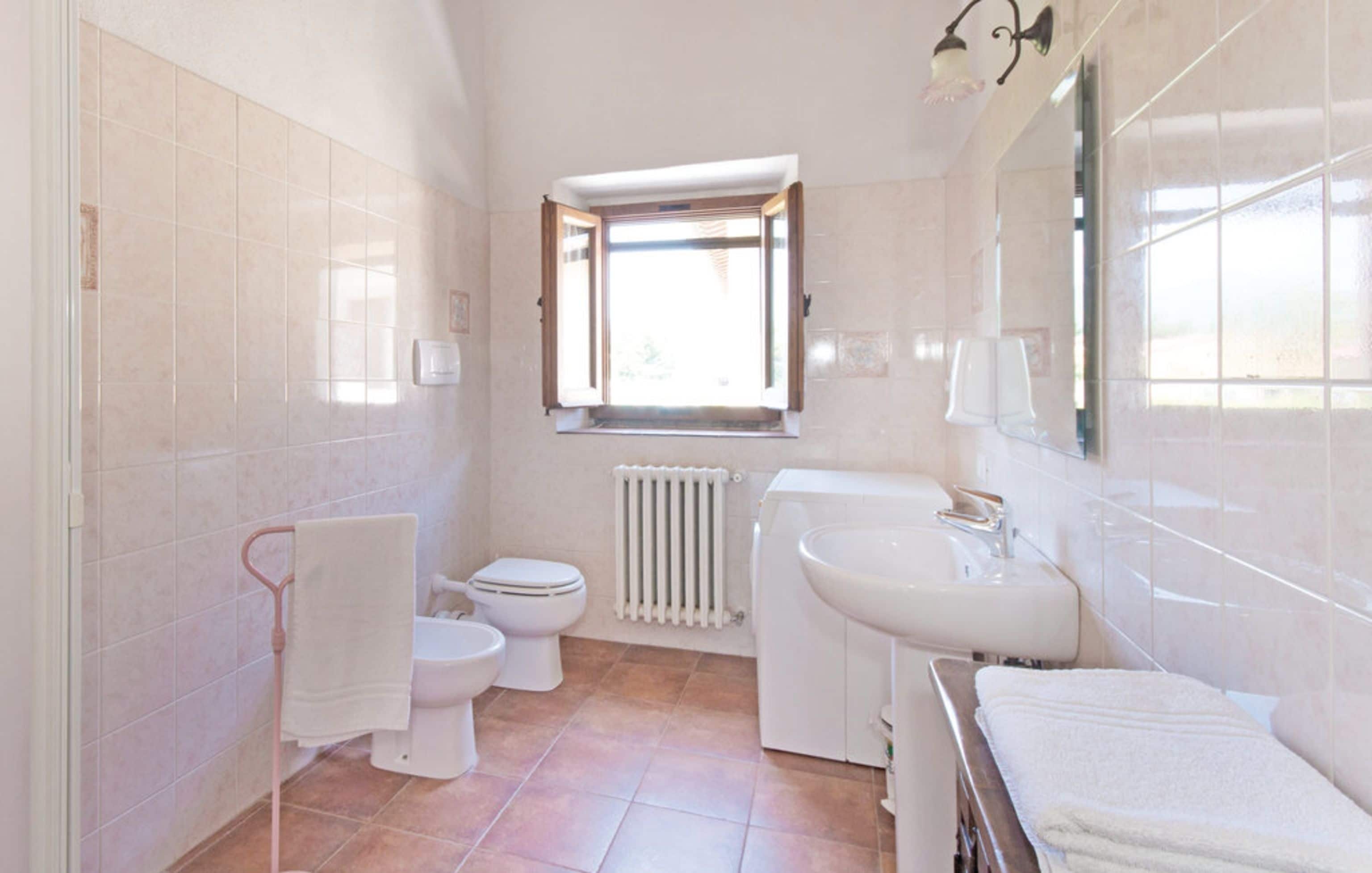 Et badeværelse med toilet, bidet, vask og et vindue med udsigt.
