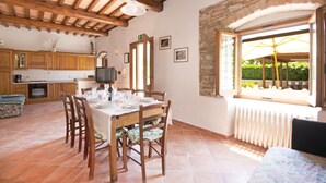 A dining area with a wooden table set for four, surrounded by chairs. A stone wall and window with an umbrella are visible. - Podere Grossi (Borgo San Lorenzo)