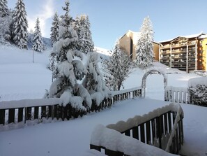 A snow-covered landscape with a wooden fence, snow-laden trees, and a building with balconies. - Le Blanchon Hotel (Selonnet)