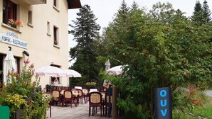 Un espacio al aire libre con mesas y sillas, un cartel que indica 'Le Blanchon Hotel Restaurant' y un cartel que dice 'OUVER'.
