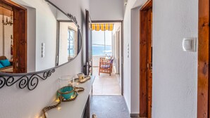 Ein Flur mit einer Holztür, einem Spiegel und Blick auf einen Balkon mit einem Stuhl und einem gelben Sonnenschirm.