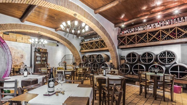Un restaurant avec des tables et des chaises en bois, des tonneaux à vin et un mur en briques.