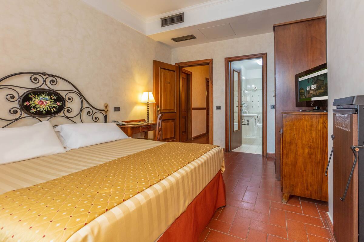 A hotel room with a bed, a desk, a lamp, a television, and a wardrobe.