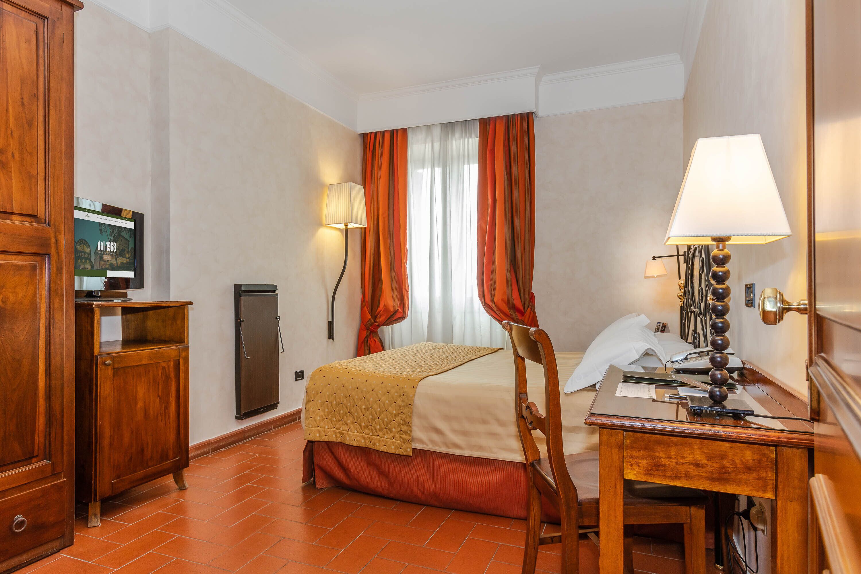 Une chambre d’hôtel avec un lit, un bureau, une chaise, une télévision, une lampe et des rideaux.