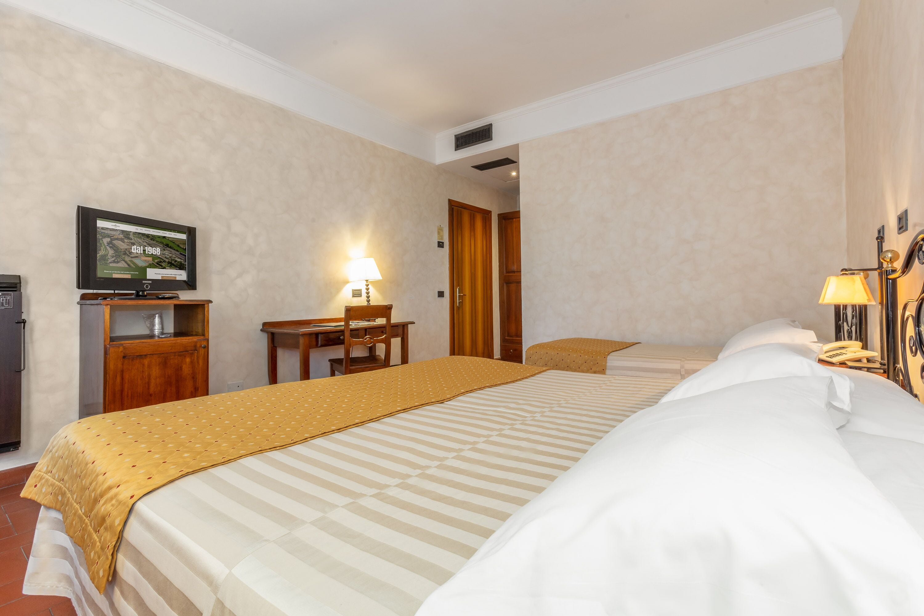 Una camera d'albergo con un letto grande, una scrivania, una sedia e una televisione appesa al muro.
