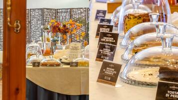 Buffet com diversos doces sob cúpulas de vidro, incluindo um bolo de pera e um brownie de chocolate.
