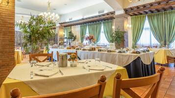 Un espace repas avec des tables rondes dressées pour les repas, entouré de murs en briques et de rideaux verts.