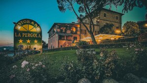 Une enseigne pour le restaurant La Pergola, situé dans un hôtel, avec une vue sur le bâtiment et sur l’espace extérieur aménagé pour les clients.