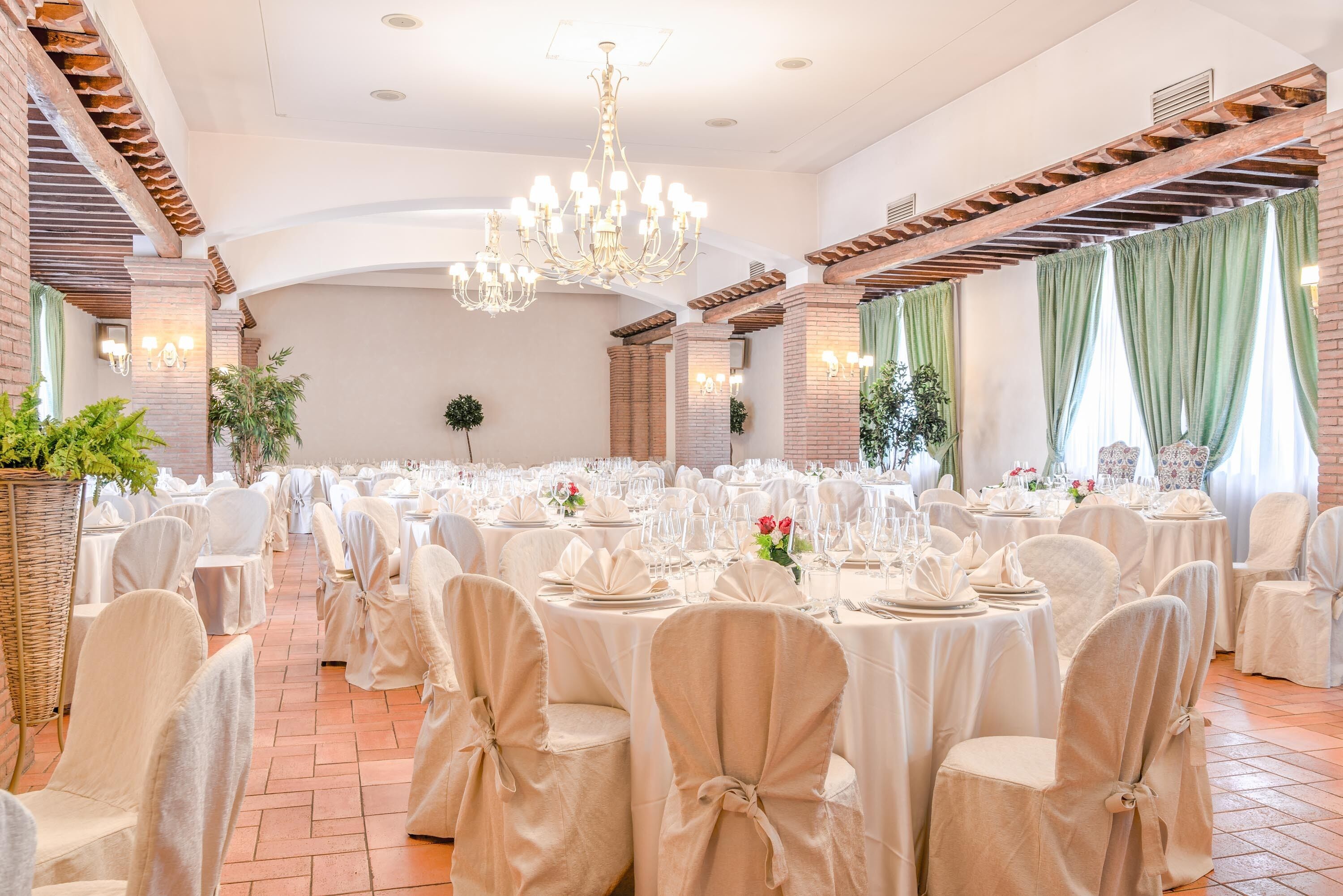 A banquet hall with round tables, chairs with white covers, a chandelier, and brick walls.