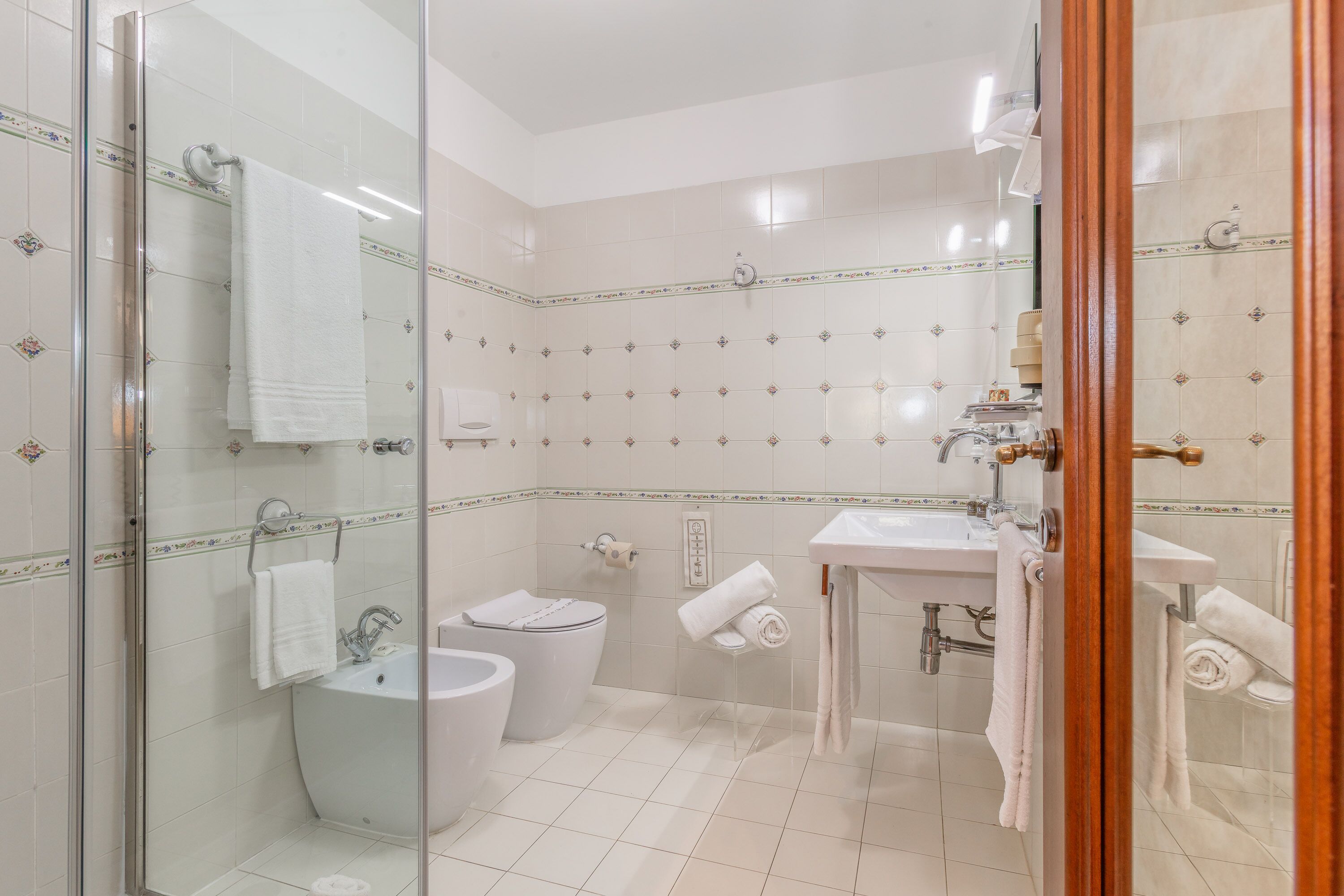 A modern bathroom with a glass shower enclosure, a toilet, a bidet, and a sink.