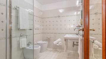 A modern bathroom with a glass shower enclosure, a toilet, a bidet, and a sink.