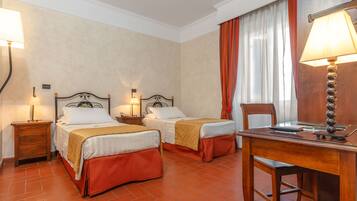 A hotel room with two beds, a desk, and a chair. There are two bedside tables with lamps.