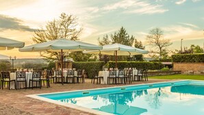 Un espace de restauration aménagé au bord de la piscine, avec des tables et des chaises, des parasols et une vue dégagée sur le paysage environnant.
