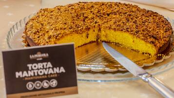 A Torta Mantovana cake with a slice cut out, placed on a glass plate with a sign beside it.