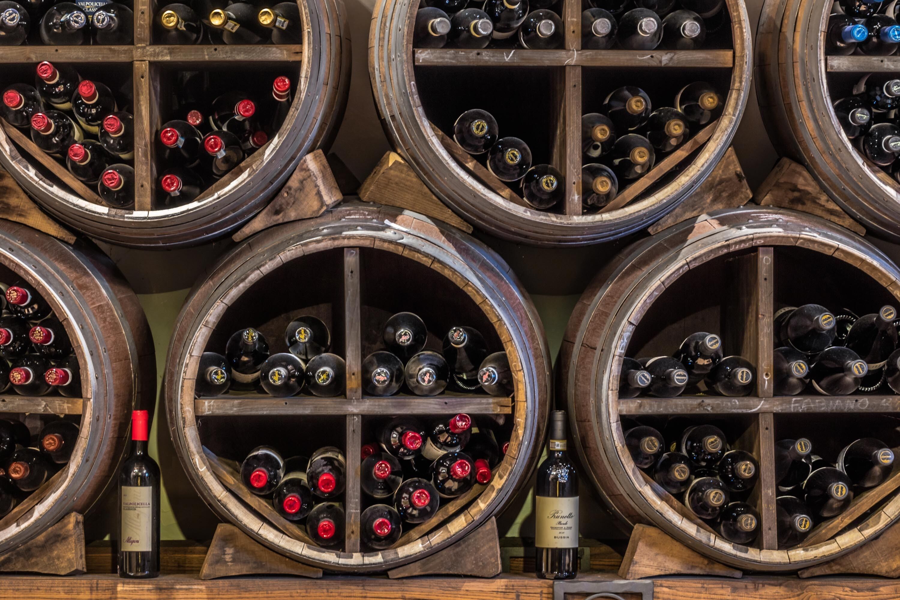 Une cave à vin où de nombreuses barriques en bois sont disposées en rangées, chacune contenant des bouteilles de vin.