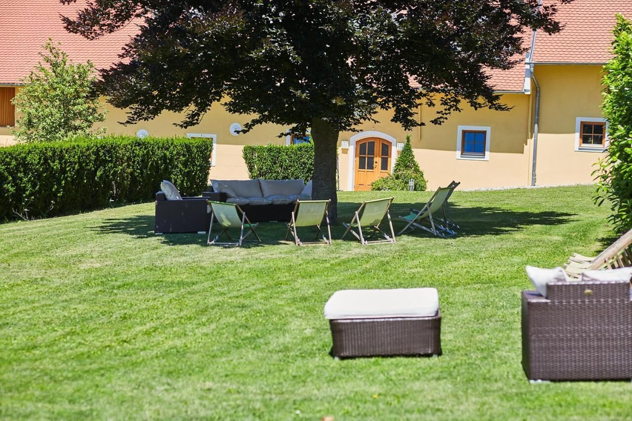 Ein gepflegter Rasen mit Gartenmöbeln, darunter eine Sitzecke und Stühle, sowie ein großer Baum, der Schatten spendet.