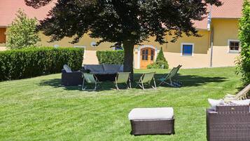 Ein gepflegter Rasen mit Gartenmöbeln, darunter eine Sitzecke und Stühle, sowie ein großer Baum, der Schatten spendet.