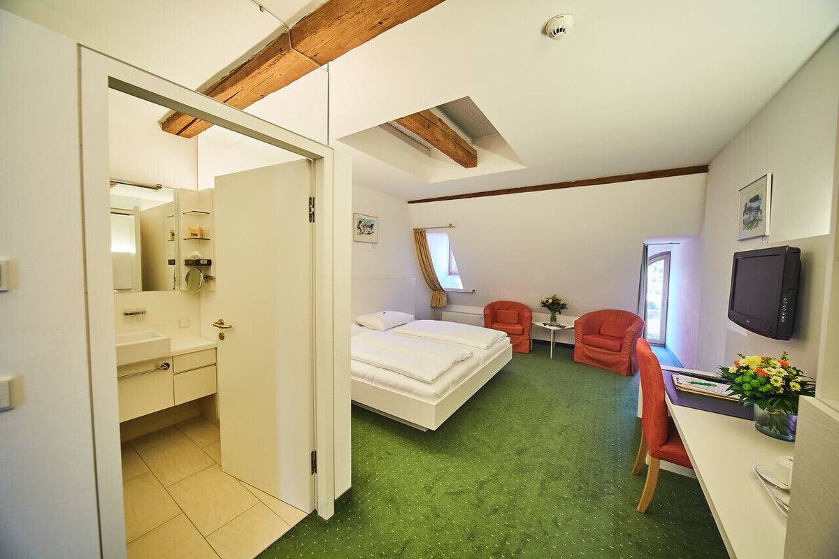 A bedroom with a bed, a desk, a chair, a TV, and a bathroom.