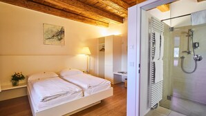 A bedroom with a wooden ceiling, a bed, a bedside table with a lamp, and a view into a bathroom with a shower.