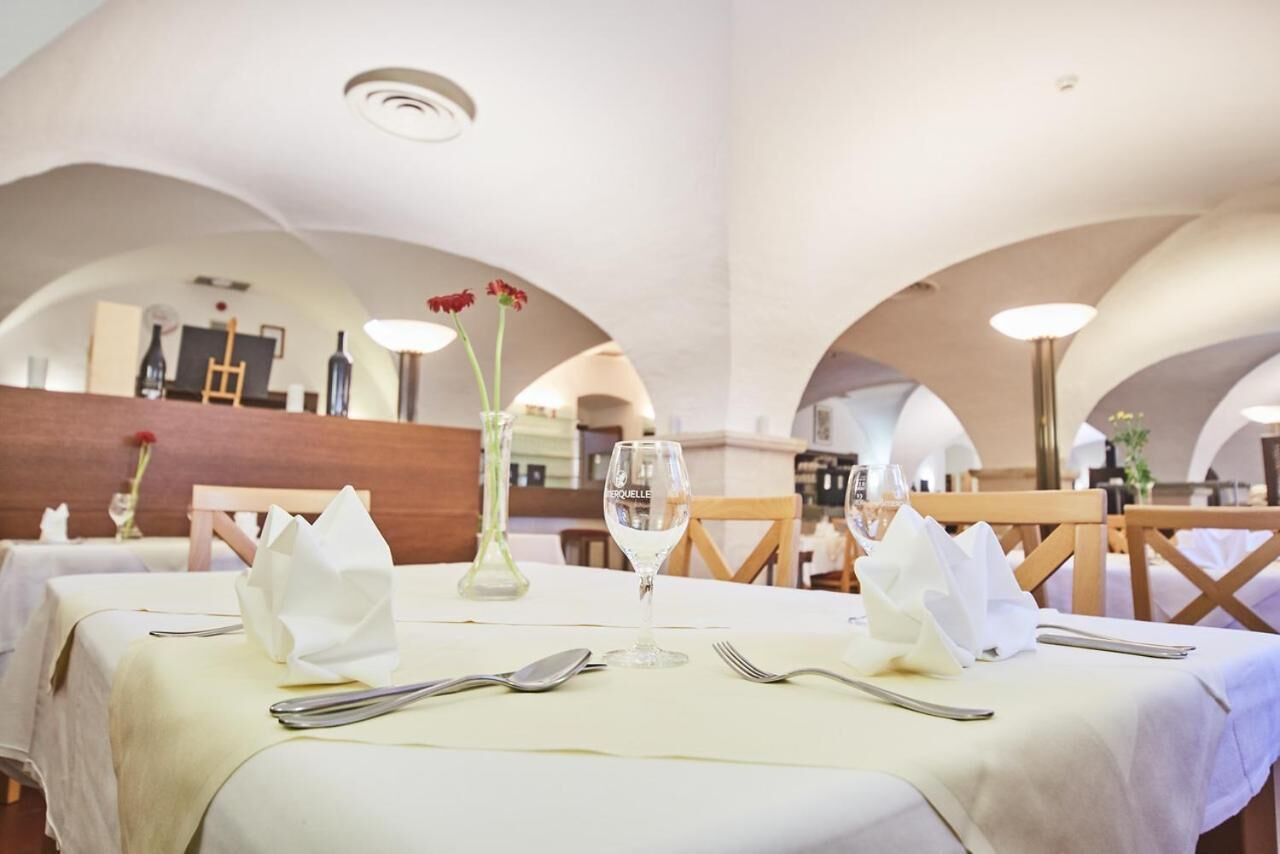A dining area with tables set for two, white tablecloths, and a vase with red flowers.