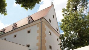 Zona d'esmorzar a l'aire lliure amb taules i caires, envoltada de plantes en testos i un edifici amb façana blanca i teulat vermell.