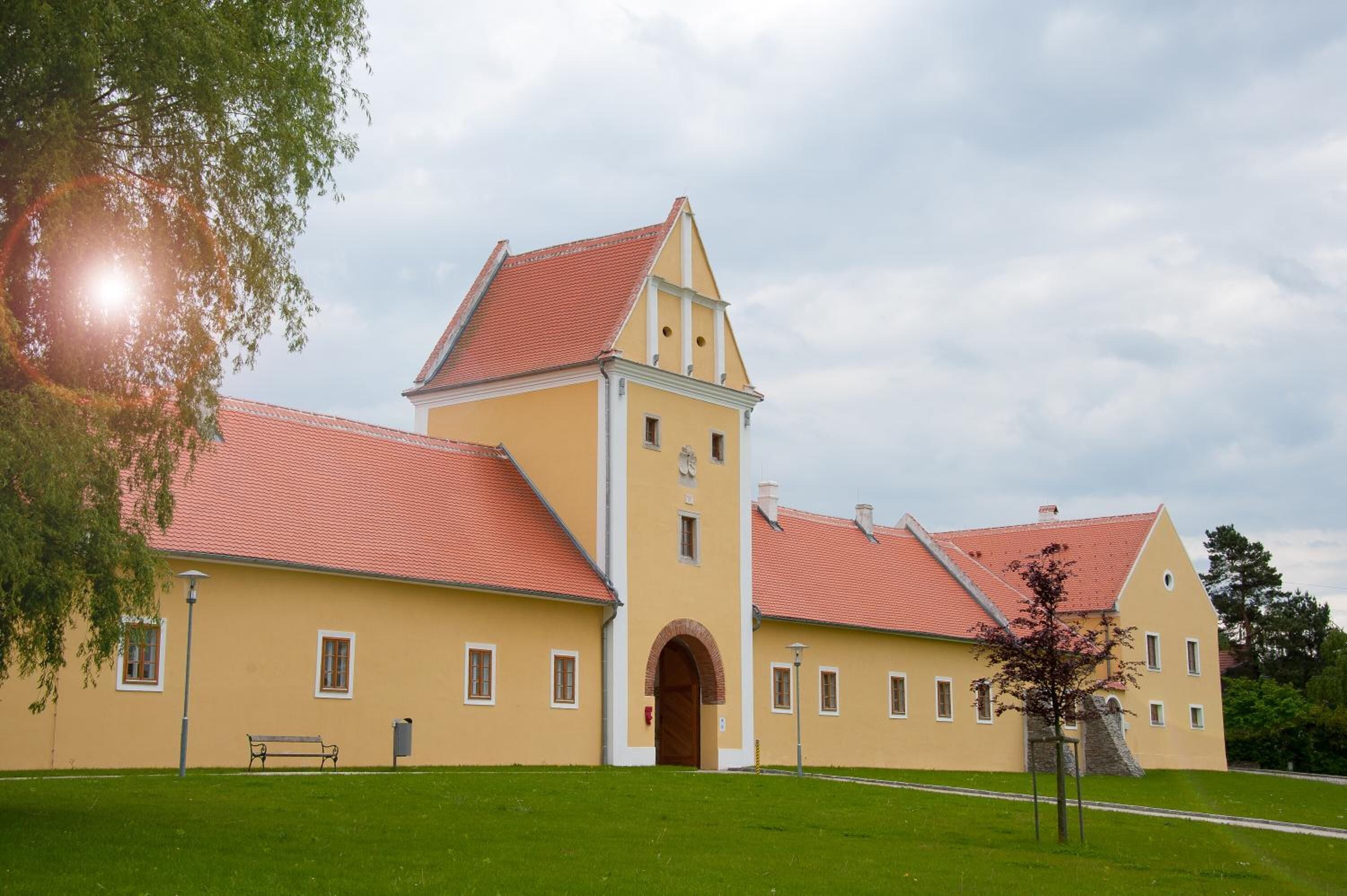 A yellow building with a red roof, a central tower, and a grassy courtyard.