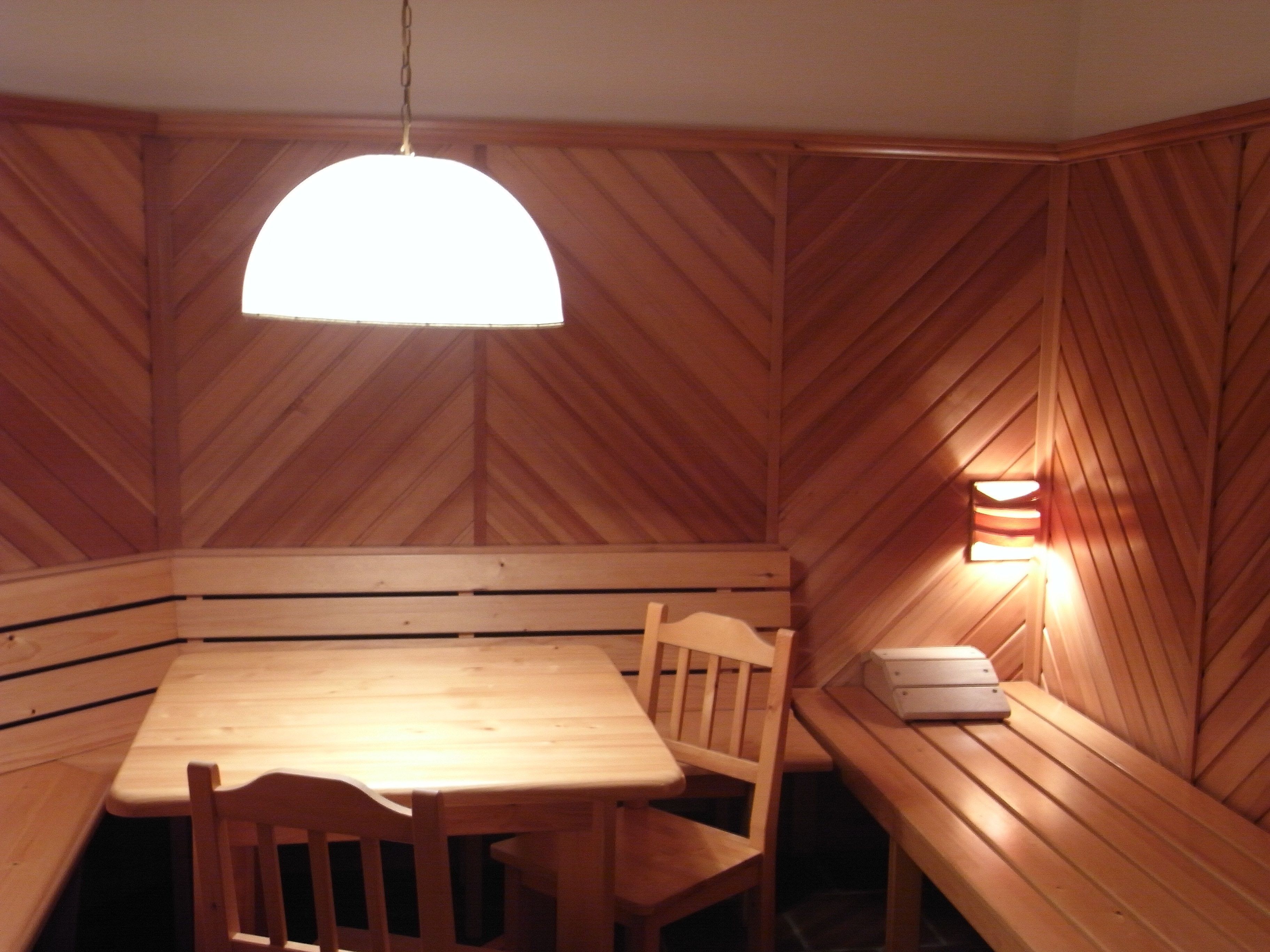 A wooden interior with a table and benches, a hanging light fixture, and a wall-mounted light.