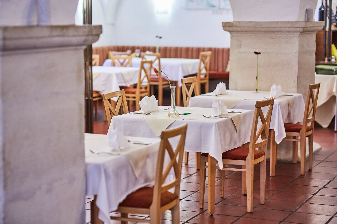 Un restaurante con varias mesas cubiertas de manteles blancos, sillas de madera y una columna de piedra.