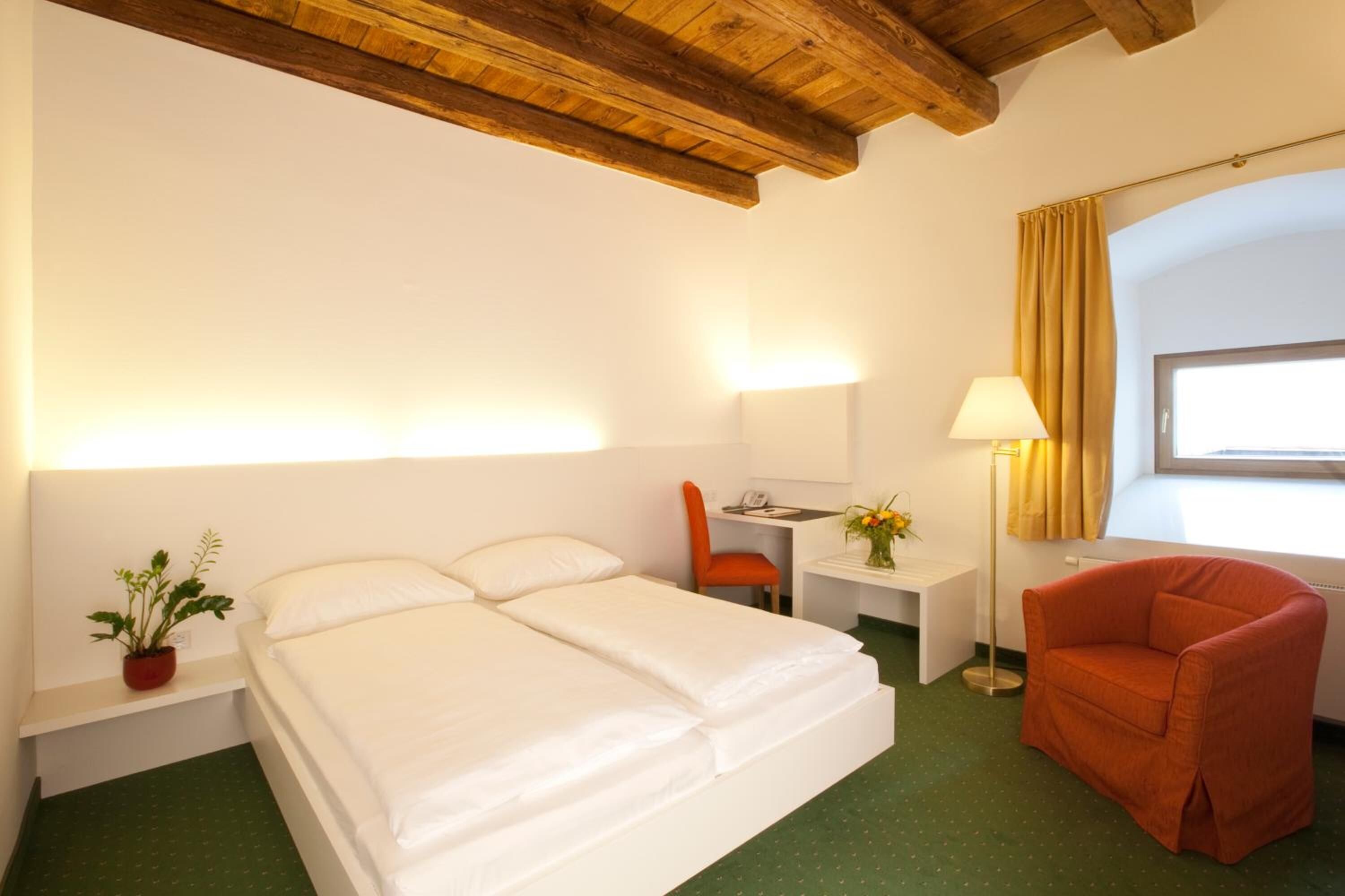 Habitación de hotel con cama, escritorio, silla, lámpara y ventana con cortinas.