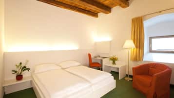 Habitación de hotel con cama, escritorio, silla, lámpara y ventana con cortinas.