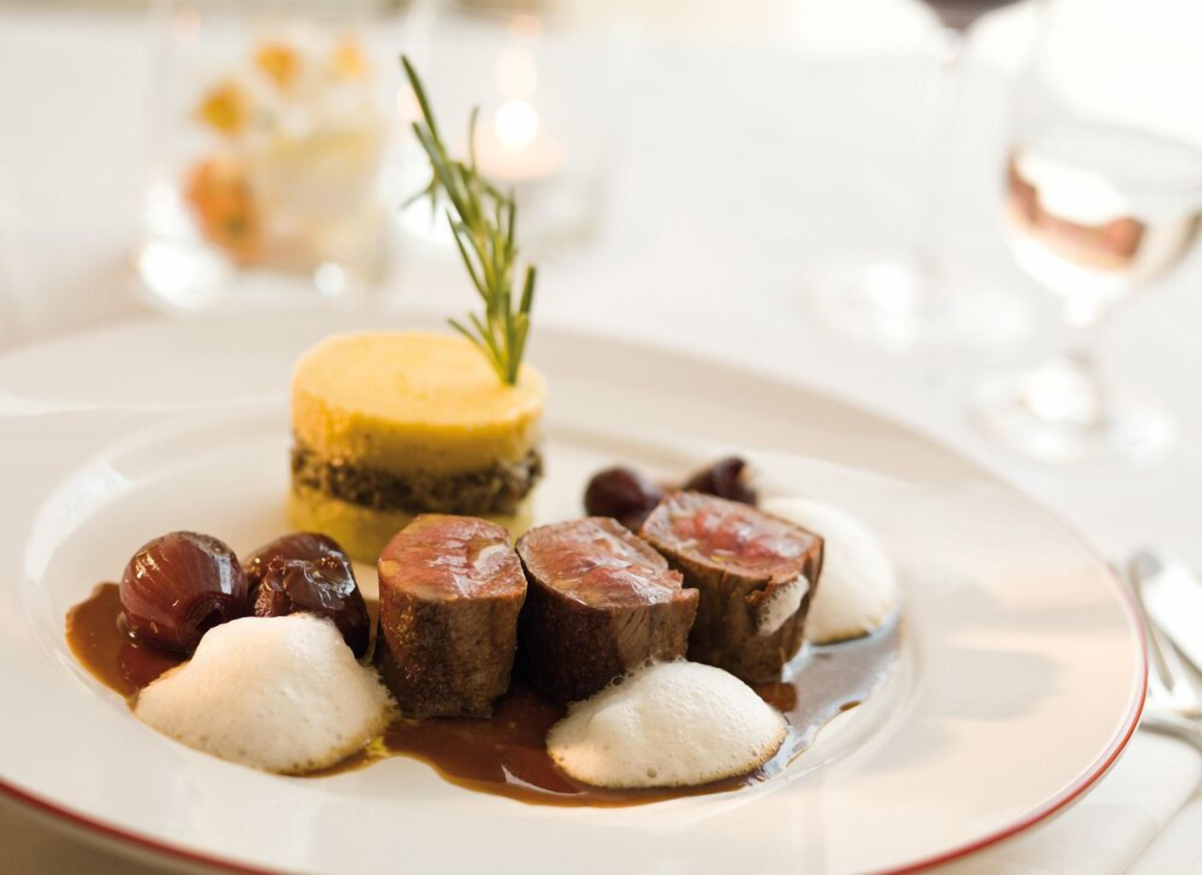 Une assiette de nourriture comprenant un dessert jaune, des boulettes blanches et des tranches de viande, le tout accompagné d’une branche de romarin.